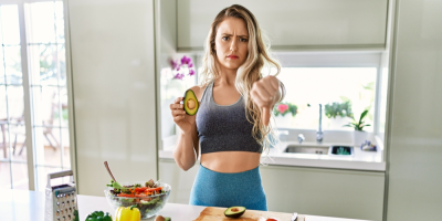 Žena drží půlku avokáda a ukazuje palec dolů