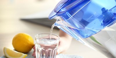 Nalévání vody z filtrační nádoby do skla v kuchyni