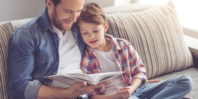 Muž a chlapec sedí na sedačce a čtou společně knihu