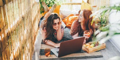 Dvě dívky ležící s notebookem na koberci na balkonu