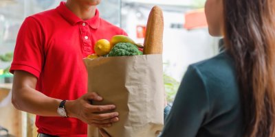 Muž předává ženě papírovou tašku s potravinami