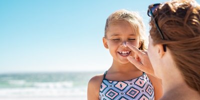 Žena maže holčičce krém na nos u moře