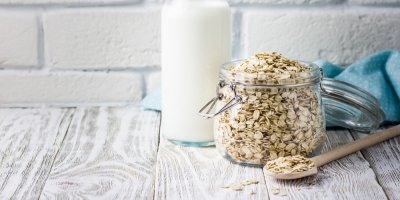 Ovesné vločky ve sklenici, láhev s mlékem v pozadí 