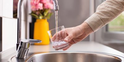 Záběr na mužskou ruku napouštějící si vodu z kohoutku do sklenice