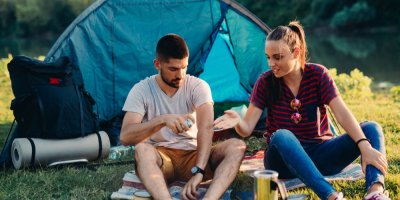 Muž a žena sedí před stanem a stříkají se repelentem.