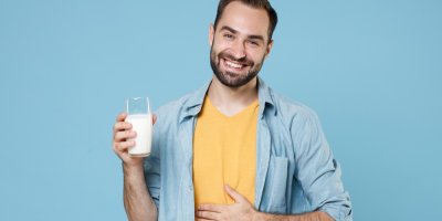 Usmívající se muž má jednu ruku položenou na břiše a v druhé drží sklenici s mlékem