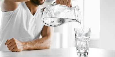 Muž nalévá vodu z džbánu do sklenice