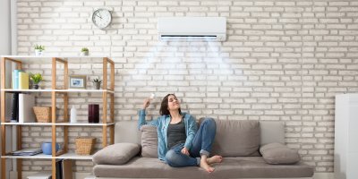 Žena sedící na gauči přepíná klimatizaci nad sebou