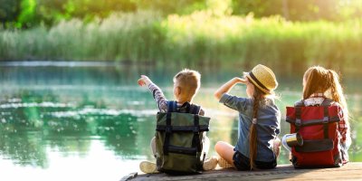 Děti s batůžky sedí u vody