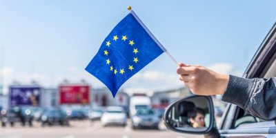 Muž mává vlajkou EU z okénka auta.