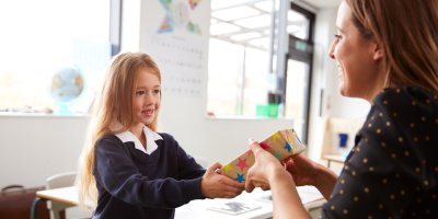 Dívka předává paní učitelce zabalený dárek