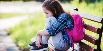 Smutná holčička s batohem na lavičce