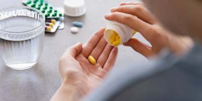 Žena si sype léky na ruku z velkého balení