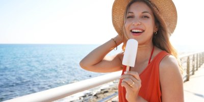 Žena v klobouku stojí u moře a drží nanuk