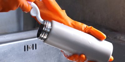 Člověk v gumových rukavicích čistí kartáčkem termosku