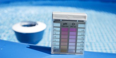 Tester vody na pH a chlór, v pozadí je bazén