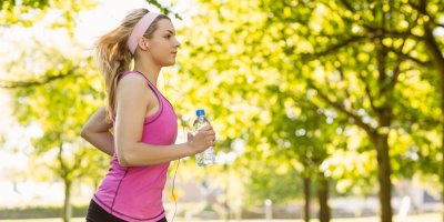 Žena běhá v parku a v ruce drží PET lahev