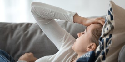 Žena leží na gauči a drží se za hlavu