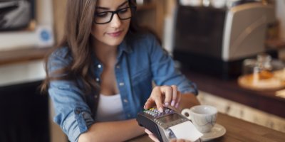 Žena zadává PIN do terminálu při platbě v kavárně