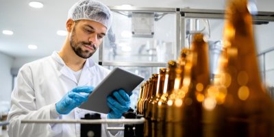 Muž v laboratoři kontroluje data na tabletu, před ním jsou lahve alkoholu