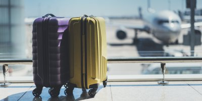 Dvojice skořepinových kufrů stojících na letišti, s letadlem v pozadí