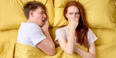 Pár leží v posteli a žena si zakrývá nos
