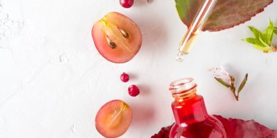 Hroznový olej v lahvičce s kapátkem, rozpůlené hrozny