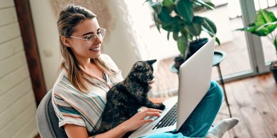 Žena pracuje na notebooku a na kolenou jí sedí kočka