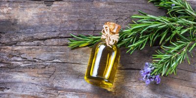 Rozmarýnový olej na dřevěné desce, pod ním větvička rozmarýnu