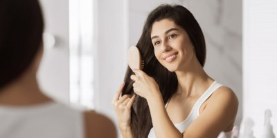 Žena si rozčesává vlasy a dívá se do zrcadla