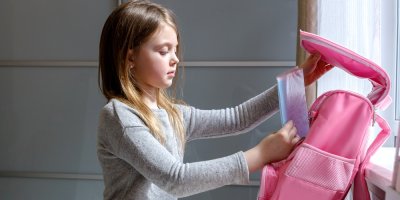 Dívka si vkládá sešit do batohu