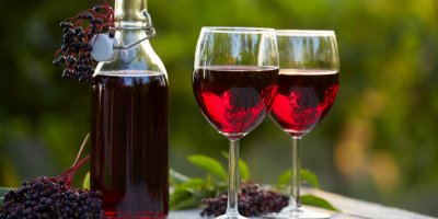 Lahev a dvě sklenice s bezinkovým vínem, plody černého bezu