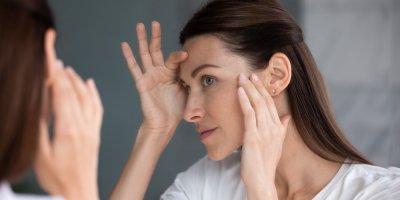 Žena si prohlíží začínající vrásky v zrcadle