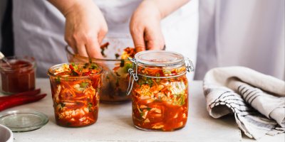 Člověk připravuje kimči v míse, před ní jsou dvě plné sklenice