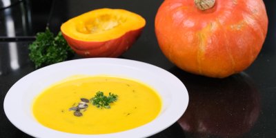 Talíř s dýňovou polévkou a dýní v pozadí