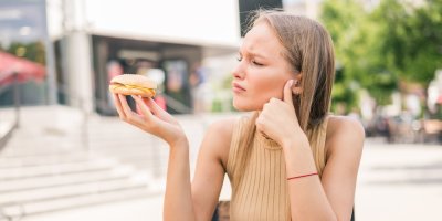 Mladá žena drží malý hamburger a smutně se na něj dívá