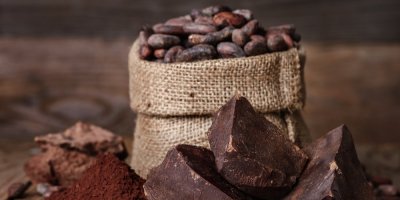 Kakaová hmota, v pozadí kakaové boby a prášek