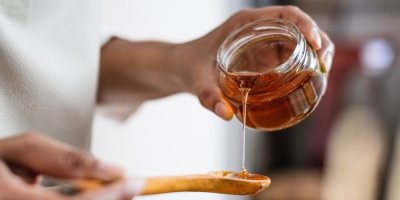 Žena nalévá med na dřevěnou lžíci