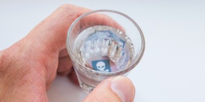 Muž drží v ruce panák, na jehož dně je lebka