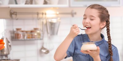 Dívka s copánky jí domácí jogurt v kuchyni