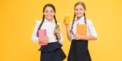 Dvě děvčata ve školní uniformě drží v jedné ruce desky a v druhé lahvičku se smoothie