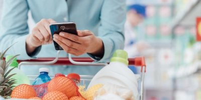 Žena se dívá do mobilu při nákupu