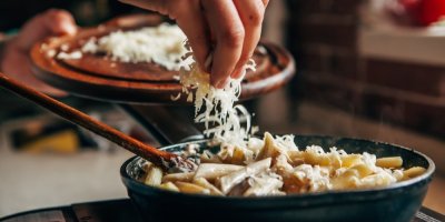 Ruce dávají nastrouhaný sýr na těstoviny