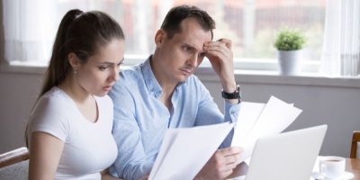 Muž a žena sedí za stolem u počítače a dívají se do papírů