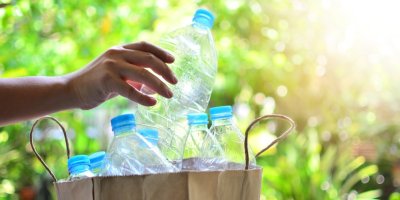 Ruka dává prázdné plastové lahve do papírové tašky