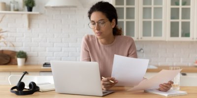 Žena drží papíry a kouká do notebooku