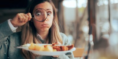 Člověk si lupou prohlíží porci jídla na talíři