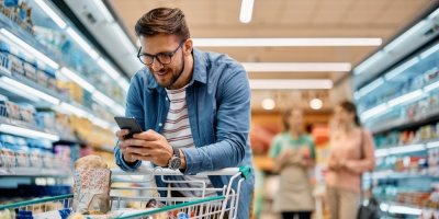 Člověk se při nakupování v supermarketu dívá do mobilu