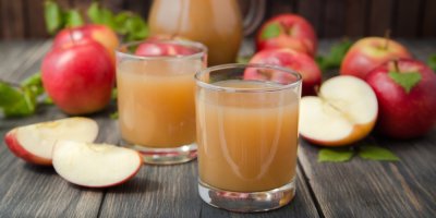 Sklenice s moštem, v pozadí nakrájená jablka