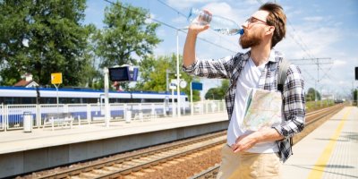 Člověk na nádraží pije vodu z PET lahve